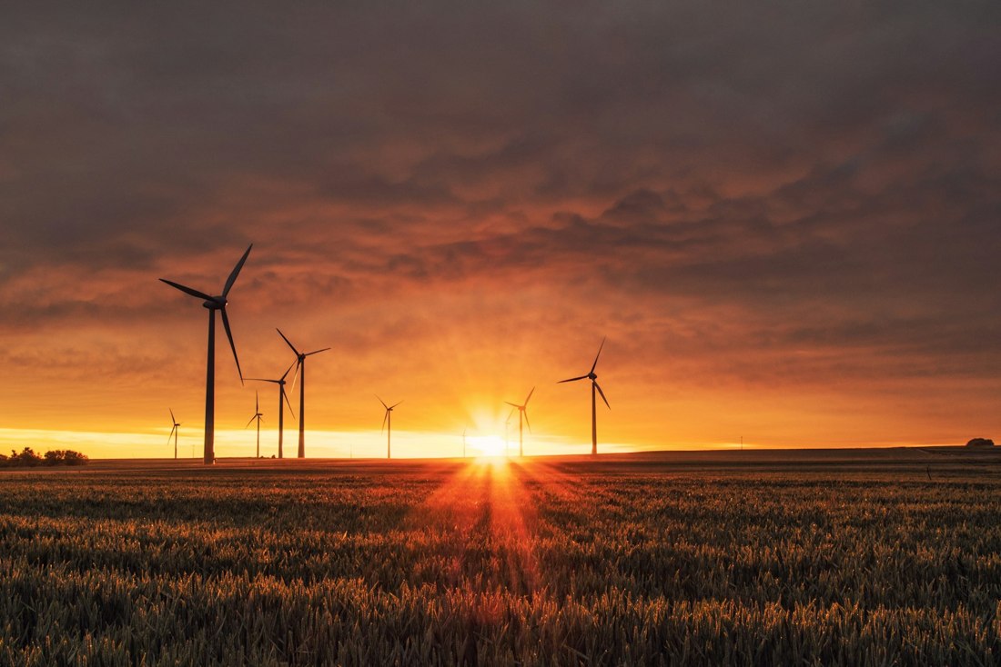 Wind turbines above farmland at sunset